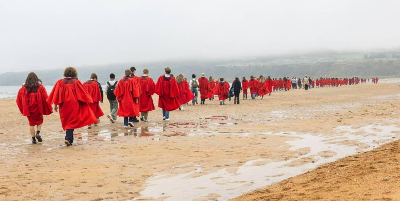 students in red gowns walking on the beach