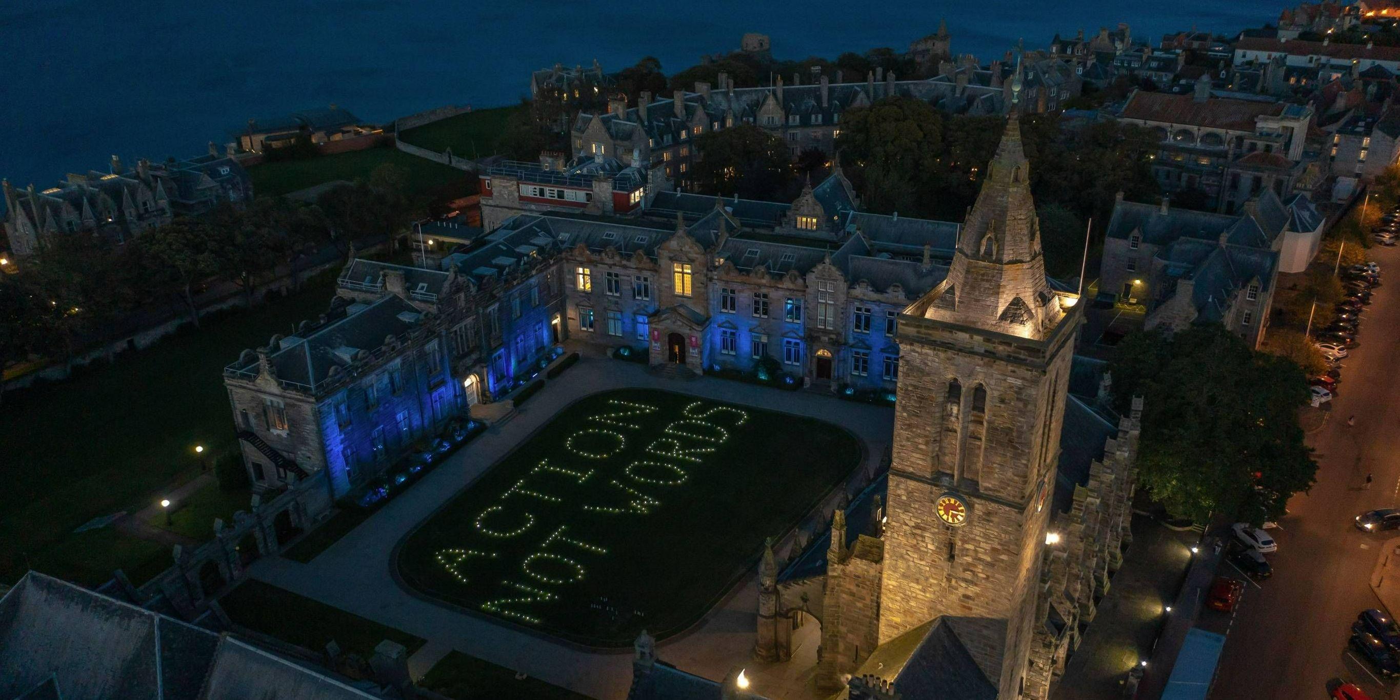 St Salvator's Quad at night lit with the phrase 'Actions not words'