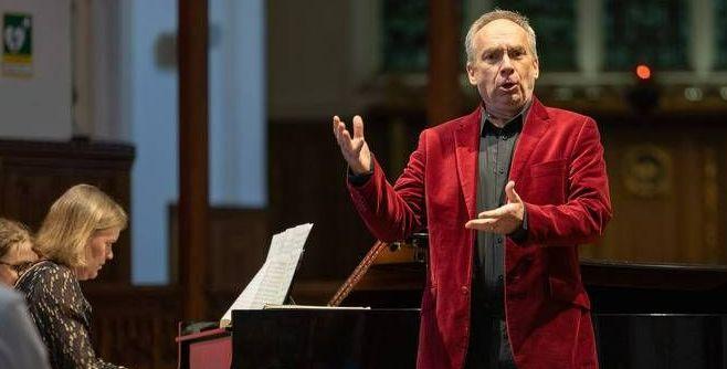 James Gilchrist can be seen singing to the right of the image, he is expressive with his hands. A pianist can be seen in the left hand corner of the image. James Gilchrist can be seen singing to the right of the image, he is expressive with his hands. A pianist can be seen in the left hand corner of the image.