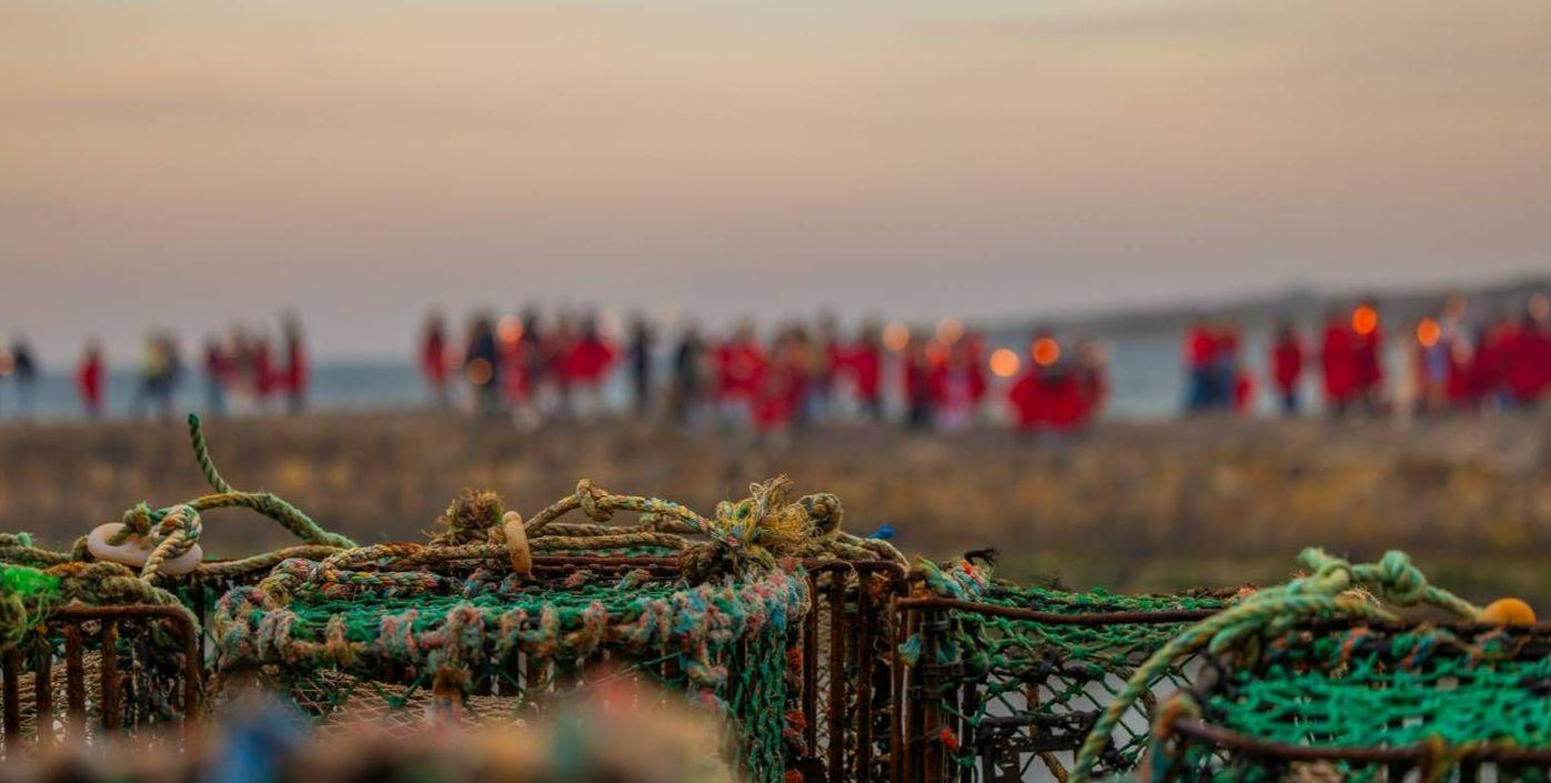 Students on the cross pier in red gowns with lobster creels to the front