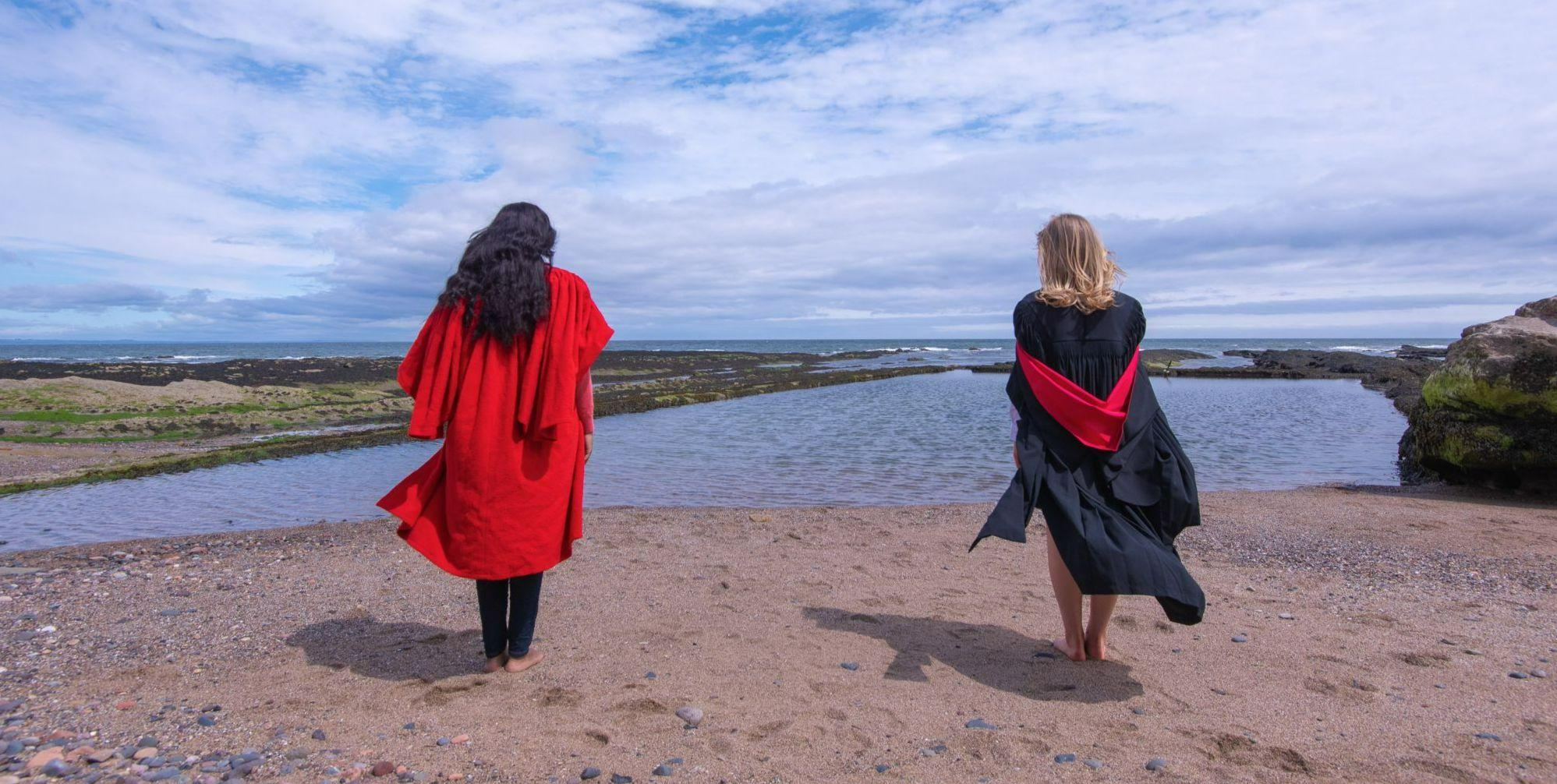 A student and a graduate in gowns on the beach