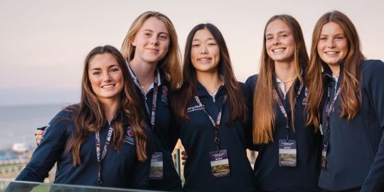 Five Saints Golf Scholars stand smiling on the terrace at Rusacks, St Andrews. They are all wearing Saints Golf kit. 