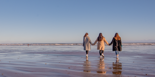 three students holding hands on beach