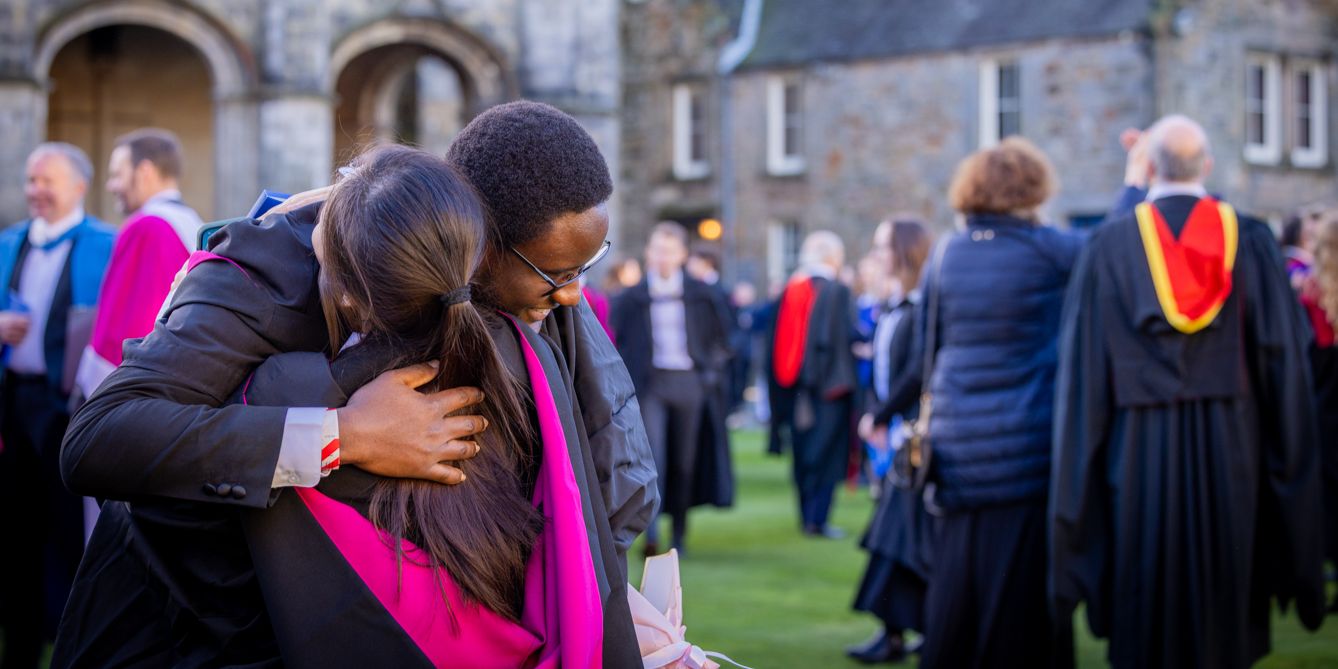 Two graduates hug during a graduation celebration in a busy St Salvator's Quad on graduation day