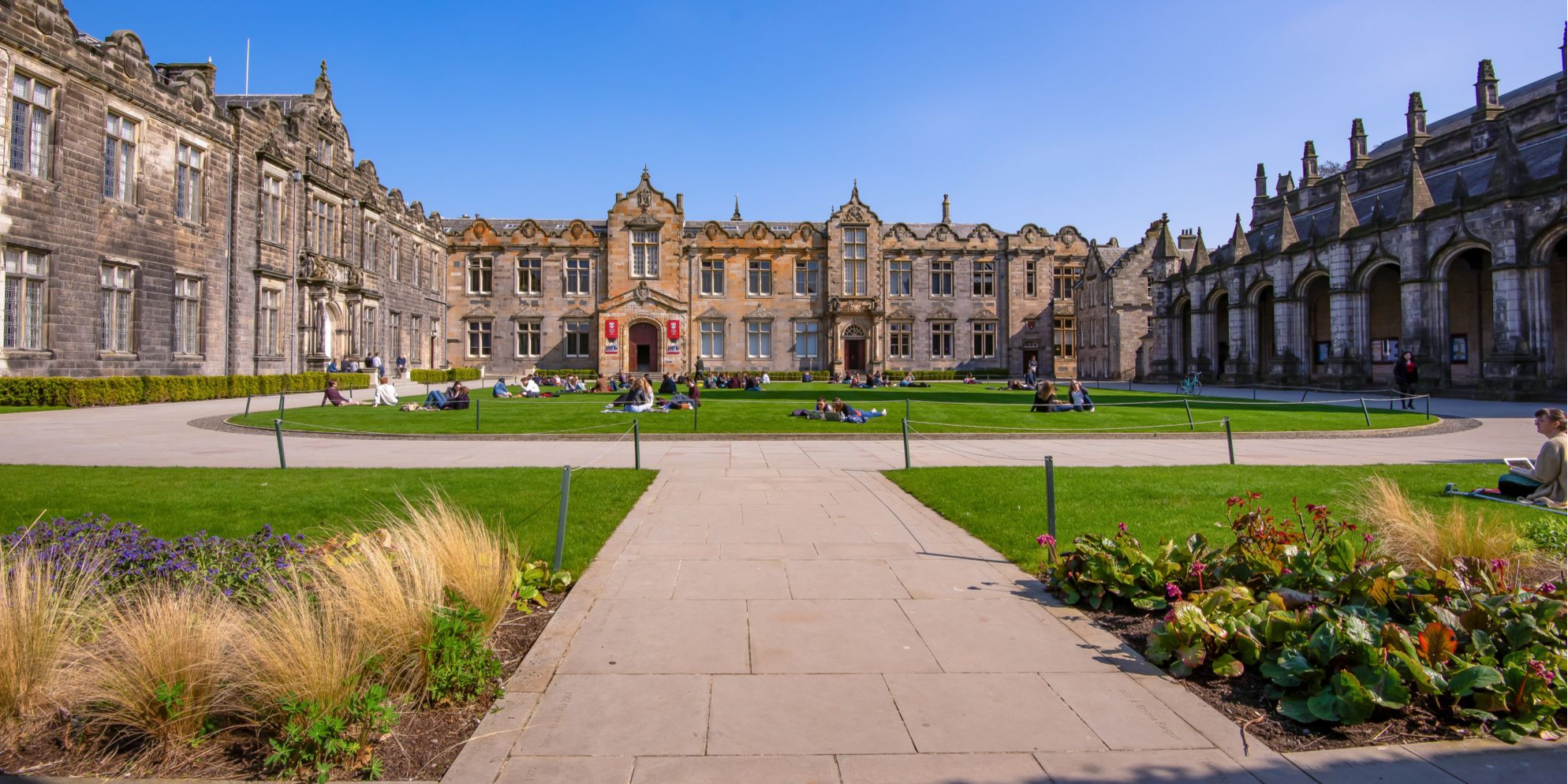 Image taken from the entrance of St Salvator's Quad on a sunny, summers day. Students can be seen sitting on the grass in the centre of the quad