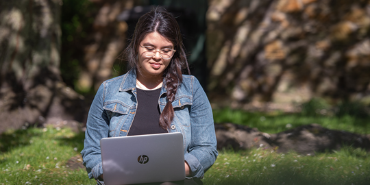 A student sits working on a laptop, sitting on the grass A student sits working on a laptop, sitting on the grass