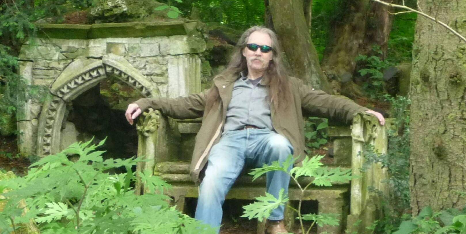 Dr John Elliott, seated on a bench in the woods Dr John Elliott, seated on a bench in the woods