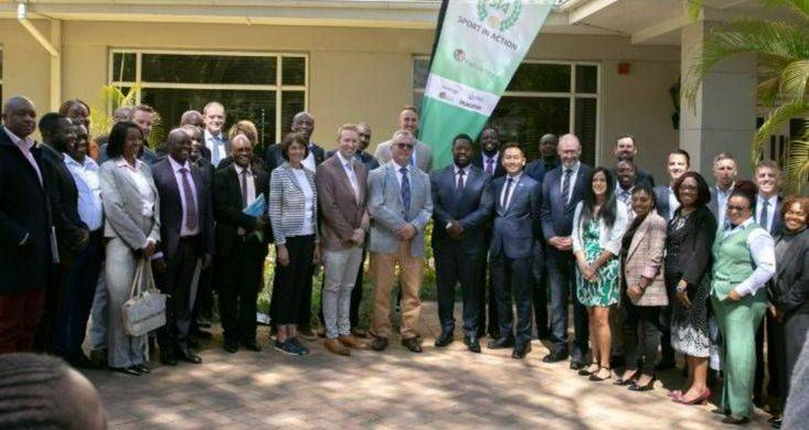 The image shows a large group of delegates in front of a green flag banner to celebrate 20 years of the Wallace Group's partnership with Sport in Action. The image shows a large group of delegates in front of a green flag banner to celebrate 20 years of the Wallace Group's partnership with Sport in Action.