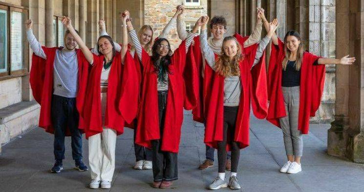 The image shows seven students wearing red gowns, celebrating in the cloister in St Salvator's Quad. The image shows seven students wearing red gowns, celebrating in the cloister in St Salvator's Quad.