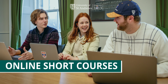 The image shows three students, two male and one female, sitting at a table with laptops featuring University of St Andrews branding. The students are smiling and engaging with one another. The image shows three students, two male and one female, sitting at a table with laptops featuring University of St Andrews branding. The students are smiling and engaging with one another.