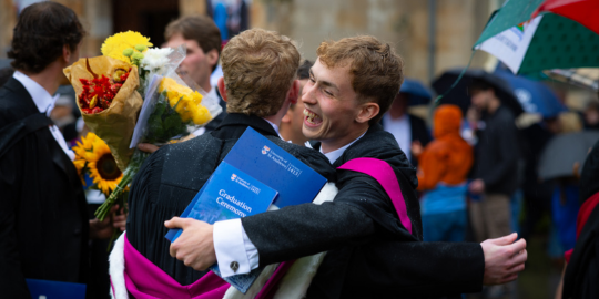 Two 2025 alumni celebrate with a hug on their graduation day 