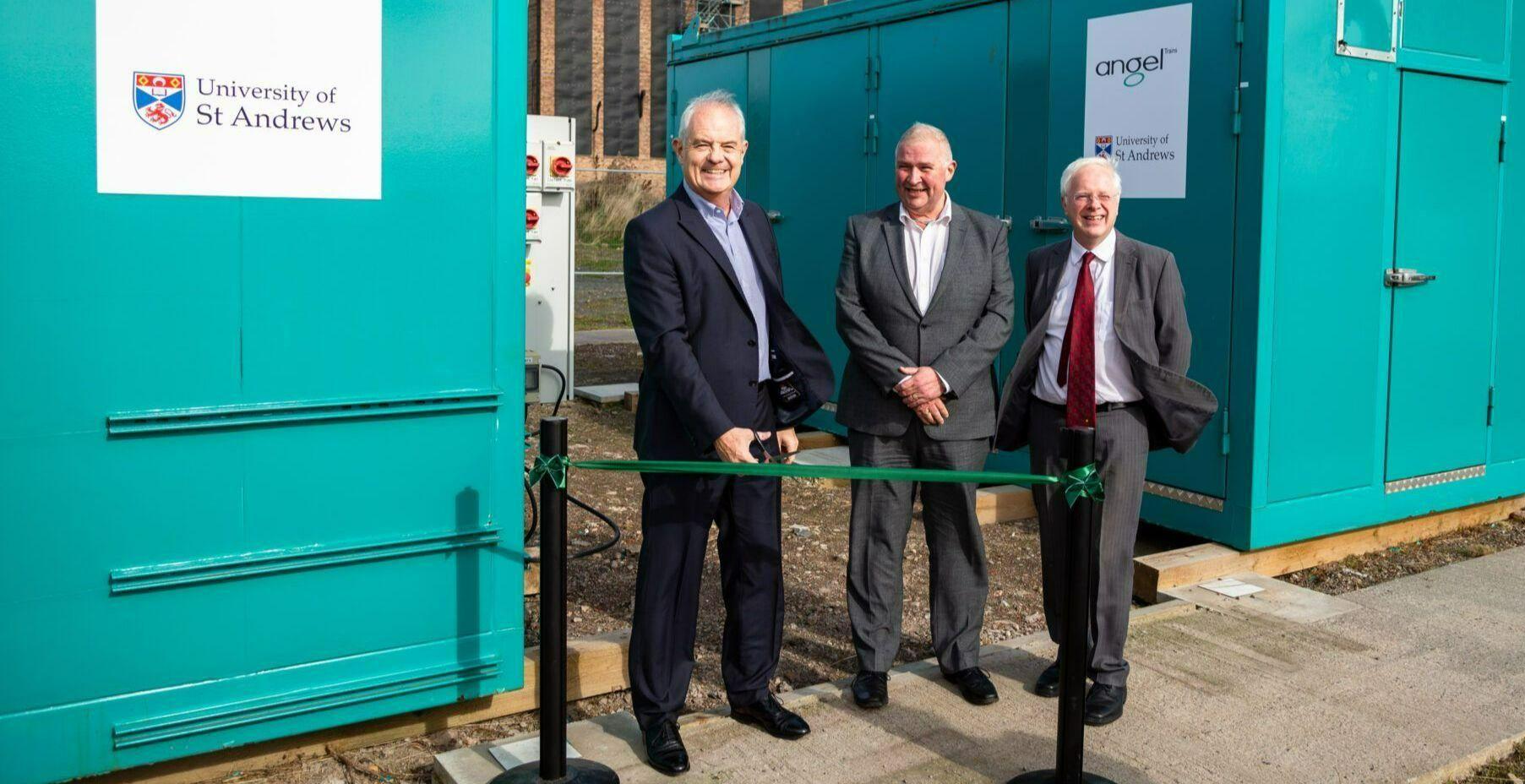 three men cutting a ribbon in front of shipping containers