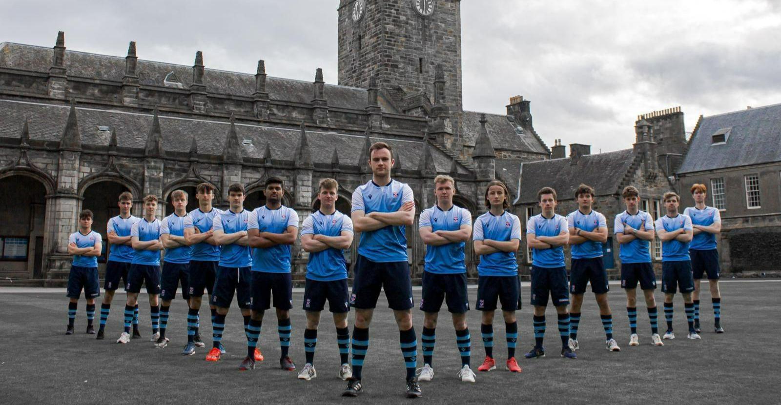 Saints Hockey men's first team standing crossed arms in their match kit, which is blue, in front of St Salvator's Chapel, which is in black and white.