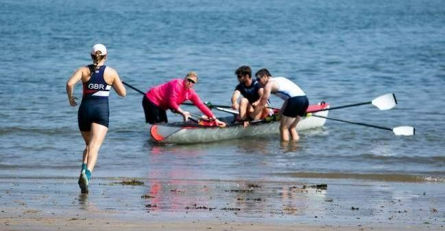 An athlete in Beach Sprints training, runs towards the boat, held in the water by teammates. 