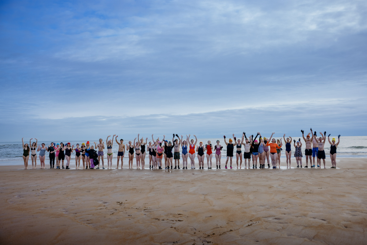 Wild swimmers cheering at the water's edge on the beach. The group is comprised of staff and students from the University of ���ϳԹ���.
